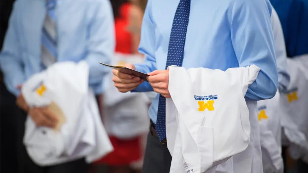 man holding white coat in hand with business shirt and tie on in blue