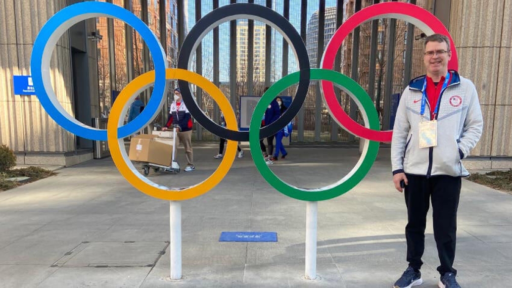 Man in white jacket standing near Olympic rings