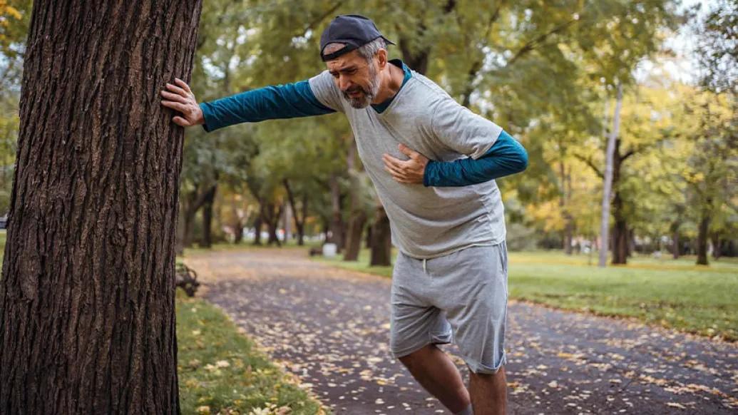 Man leaning against tree by road grabbing his chest