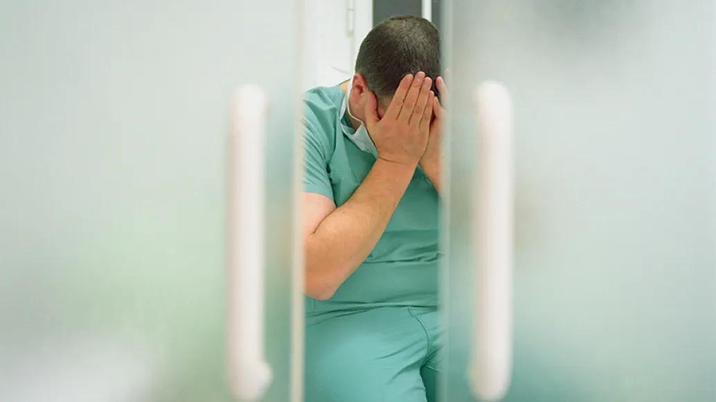 man scrubs holding hands over face sad through door