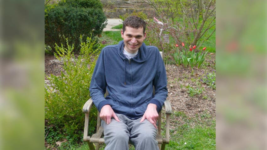Man sitting in wheel chair by garden of flowers smiling