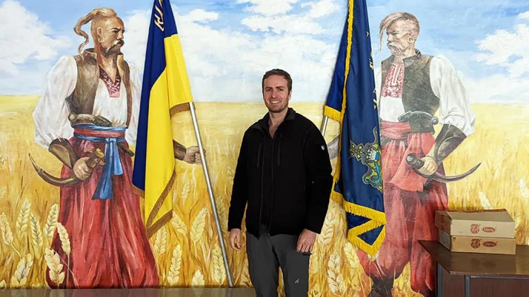 Man smiling with mural Ukraine flags in background.