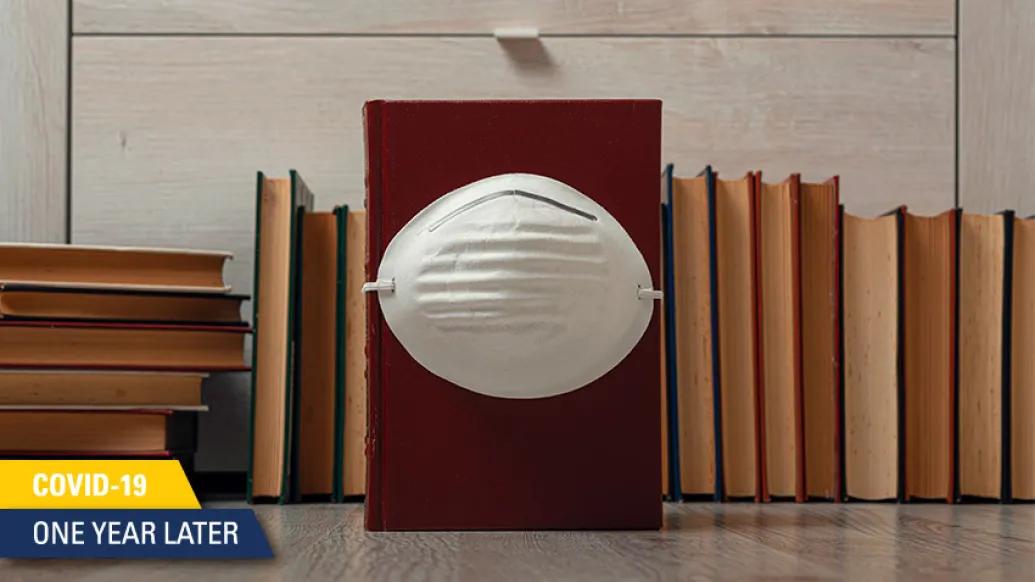 mask on brown books with covid anniversary stamp on bottom left in yellow and blue