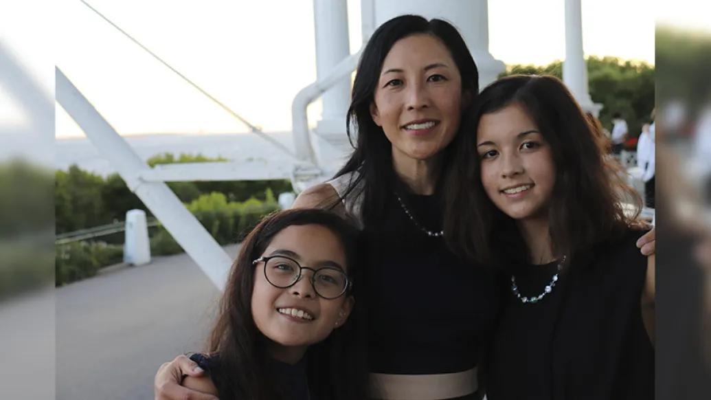 two daughters and mother smiling at camera outside on white bridge wearing black