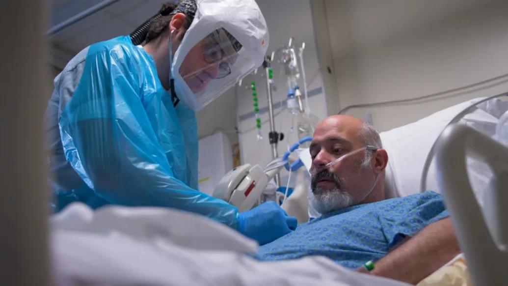health care worker with patient in bed with COVID suiting on