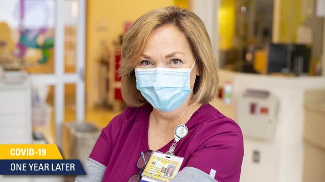 nurse in maroon scrubs and light blue mask smiling at camera