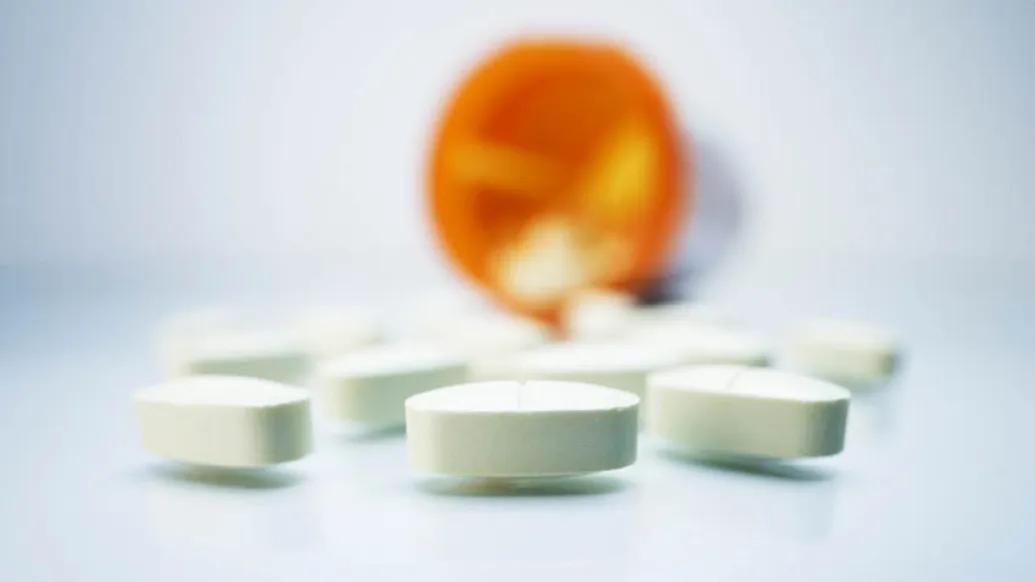 Pills spilled out of orange bottle on white surface.