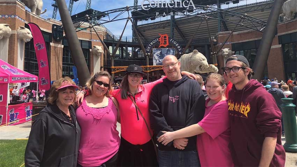 Group in pink, purple and black clothing celebrating, Detroit Tigers Comerica Park in background.