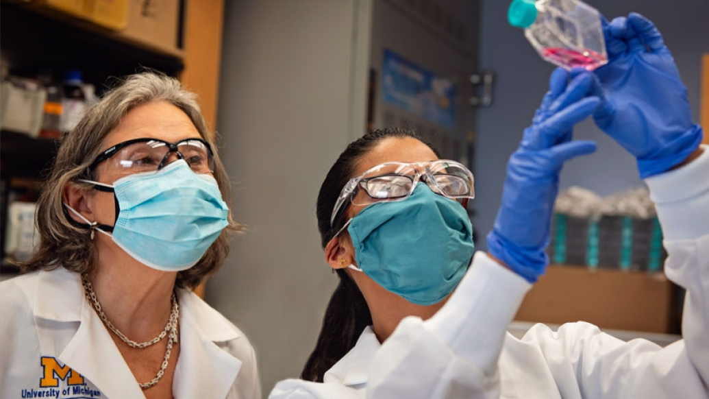 scientists in goggles gloves looking at specimen in lab 