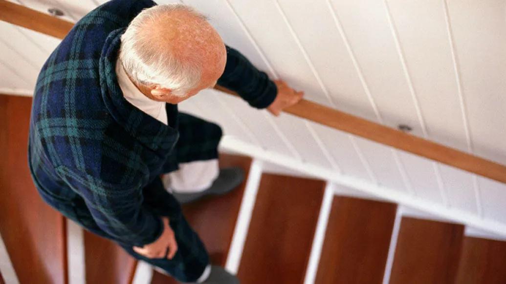 Senior man bending while walking down wooden stairs holding onto rail