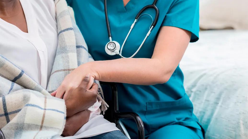 senior patient holding arm and hands with nurse with blue scrubs on