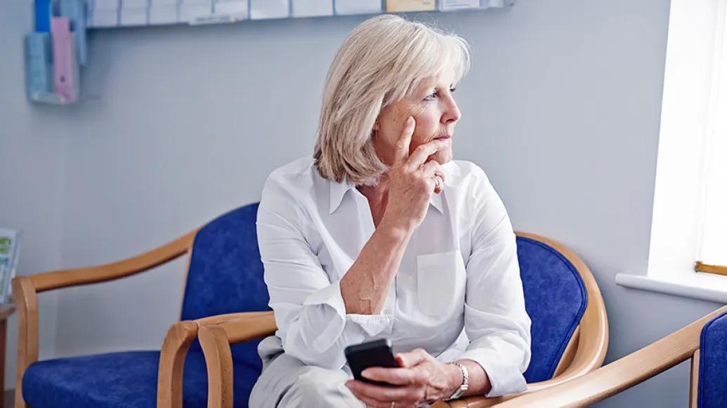 older woman sitting in chair looking at window in white shirt