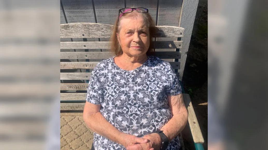 senior woman sitting smiling on bench in blue floral shirt