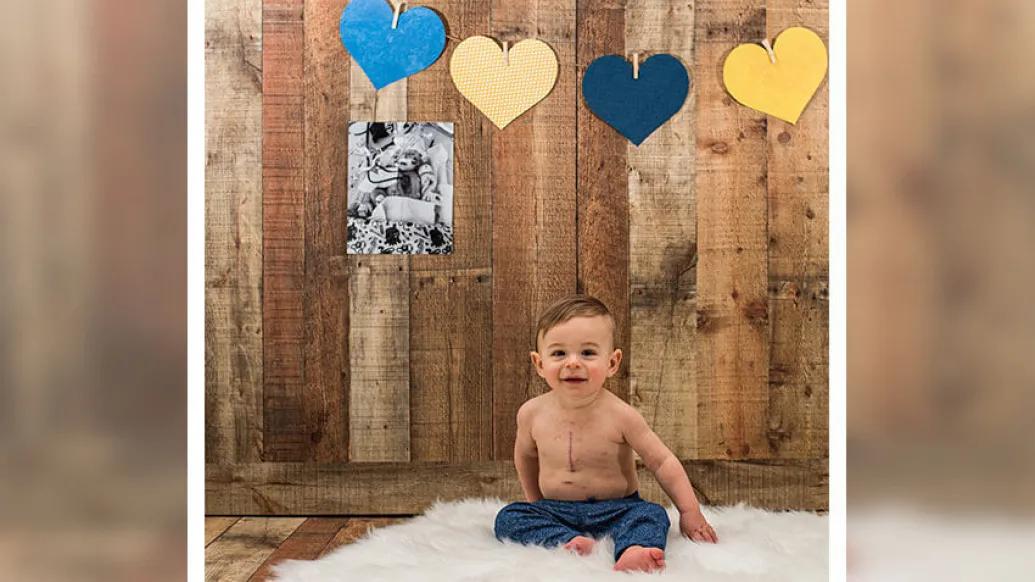 Baby smiling while sitting on fuzzy white rug, hearts and picture on wood background