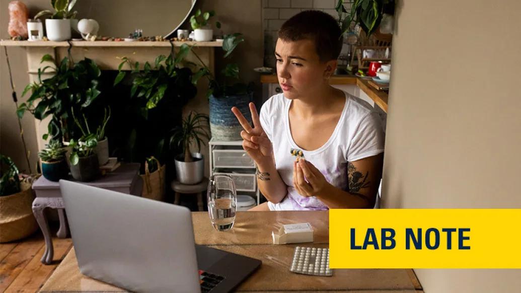 teen sitting on laptop with pills in hand in kitchen