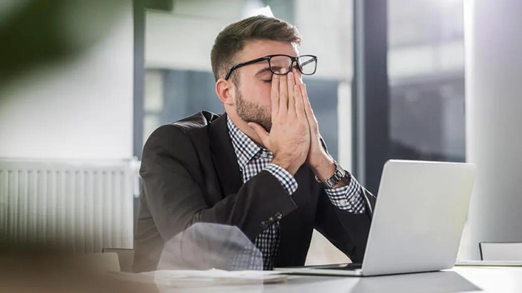 Tired man with hands on face leaning on desk while at work