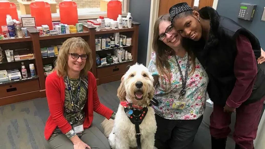 two women hugging dog and patient smiling for camera