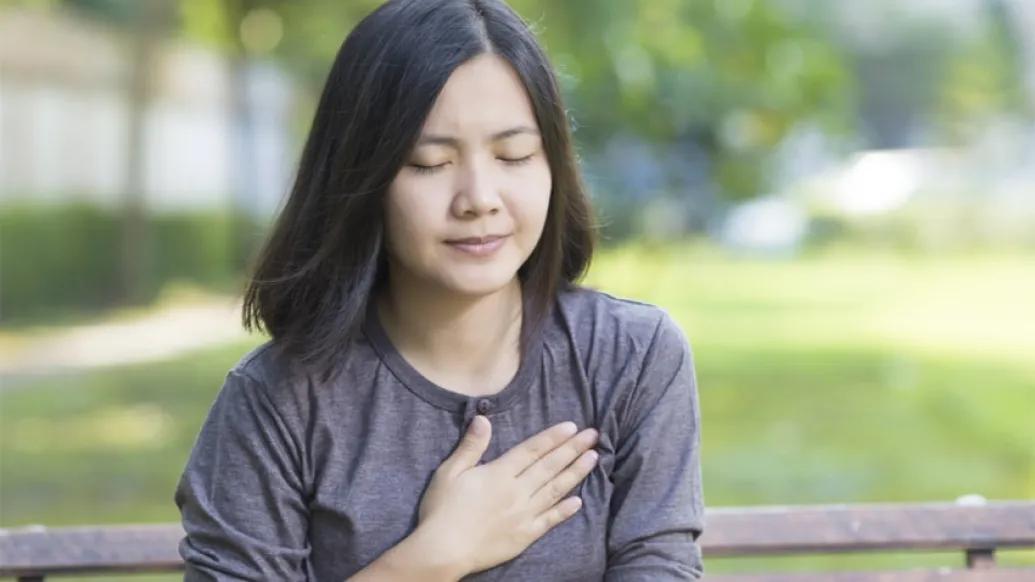 woman holding chest with hand sitting on park bench