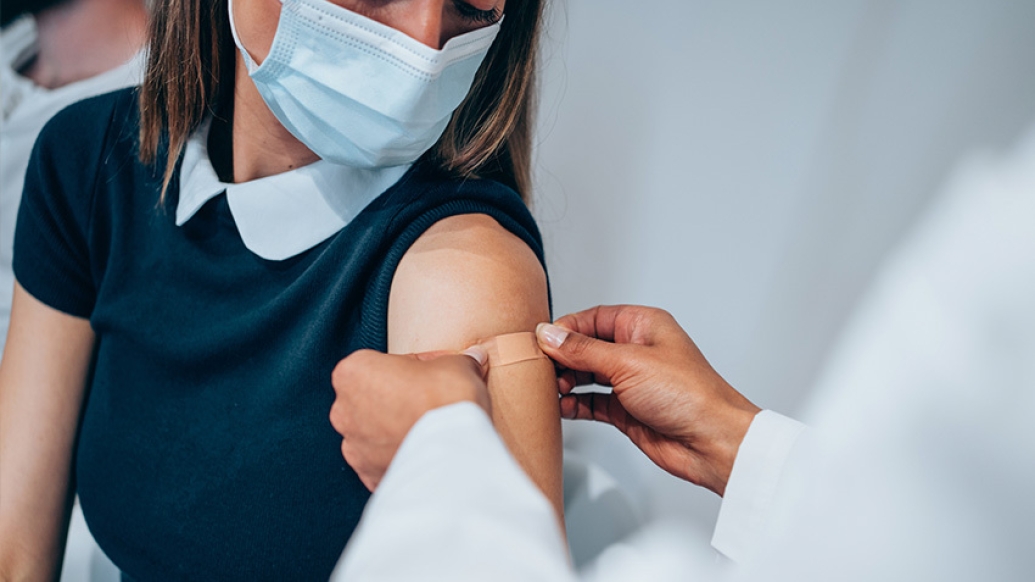 girl with navy shirt and white collar getting band aid put in arm with mask on