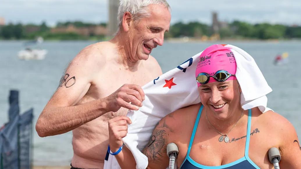 father drying off daughter on head with white towel with daughter wearing swim cap and goggles.