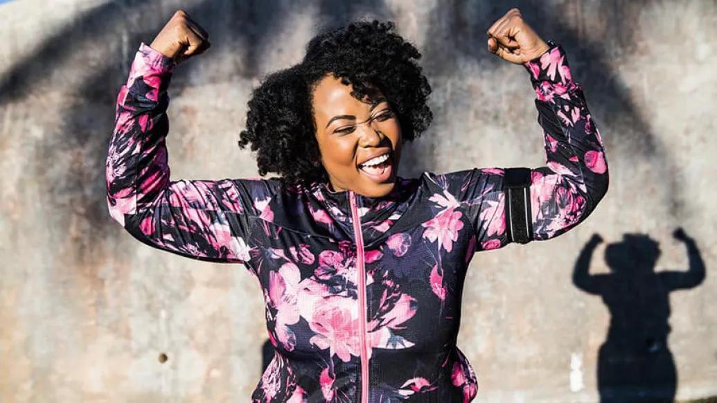 Woman in mauve zip up sports jacket with arms raised smiling