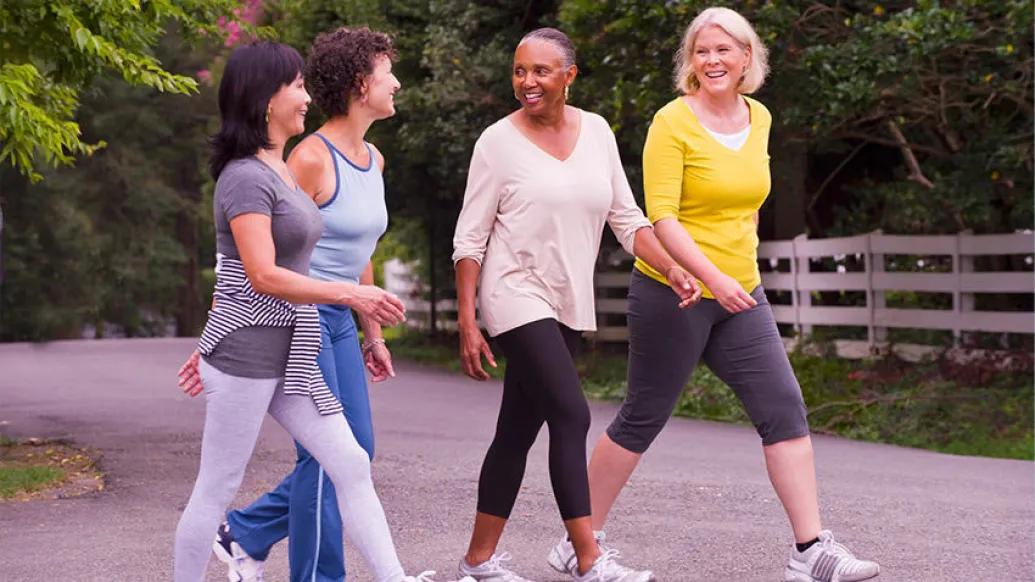 Four women walking outdoors on trail smiling