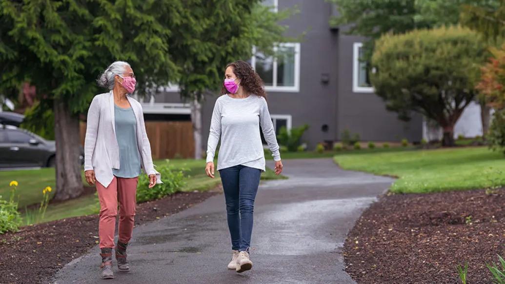 women walking outside on black path with masks on talking