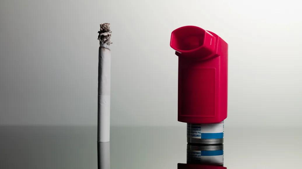 burning white cigarette and red inhaler grey background