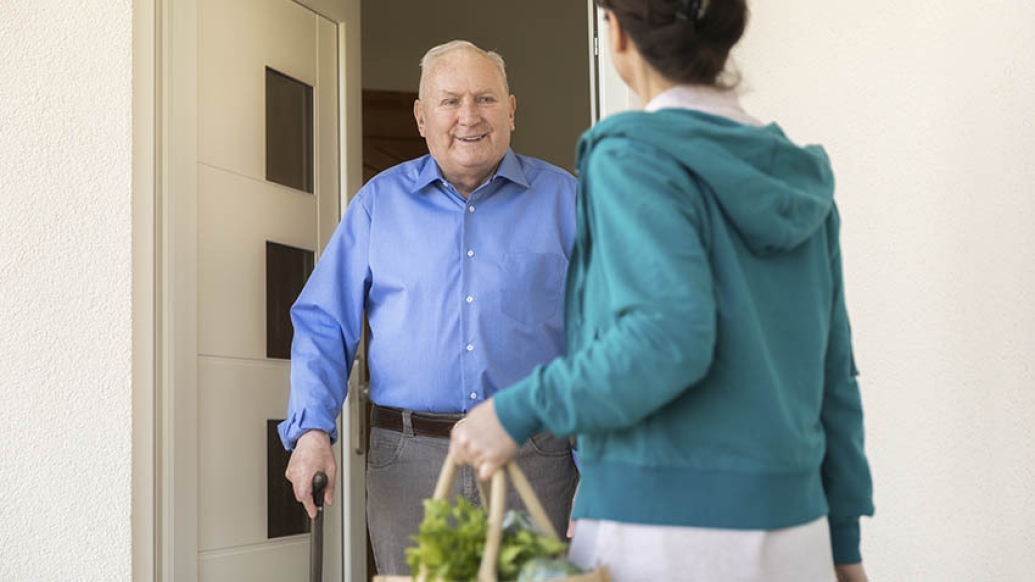 caregiver giving groceries to elderly gentleman