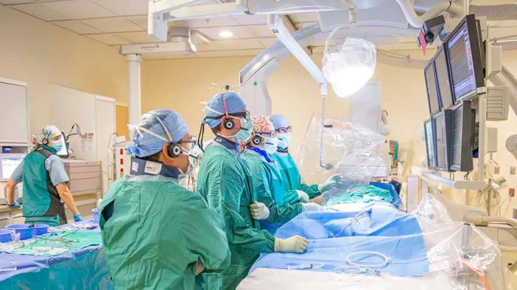Doctors and nurses in surgery room performing surgery and looking at monitors.