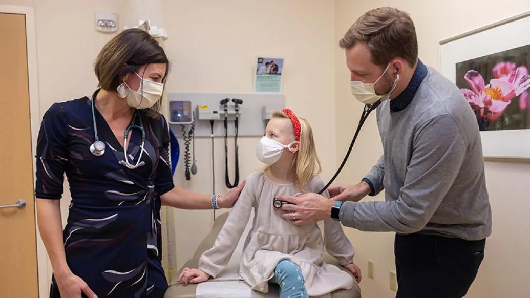 doctors with blonde child in exam room checking heart