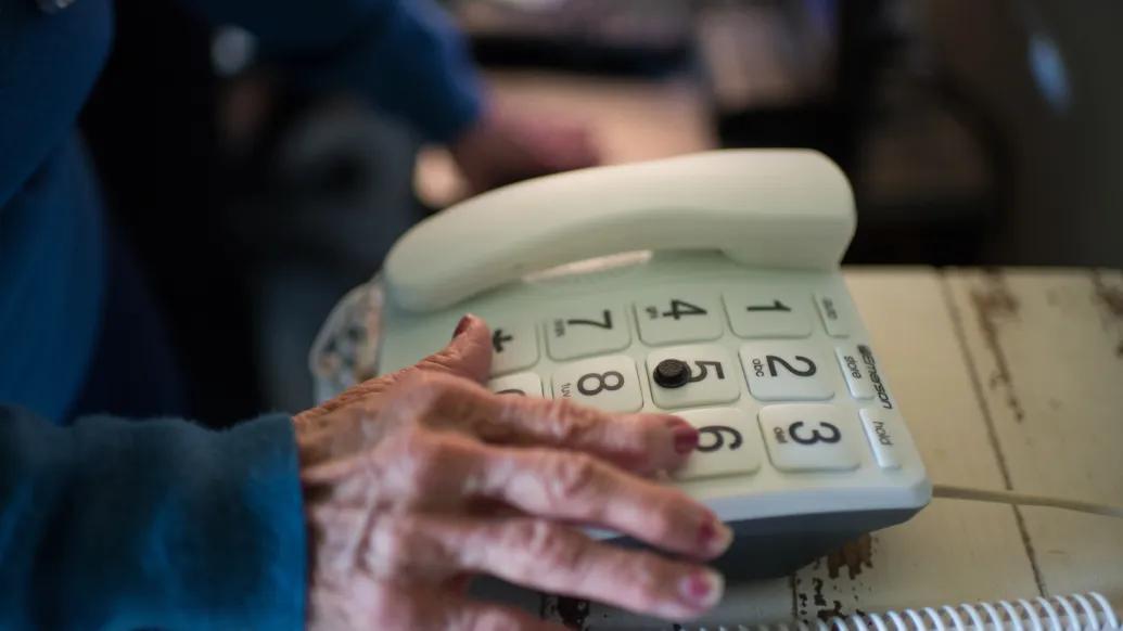 An elderly hand reaches for a large-button telephone.