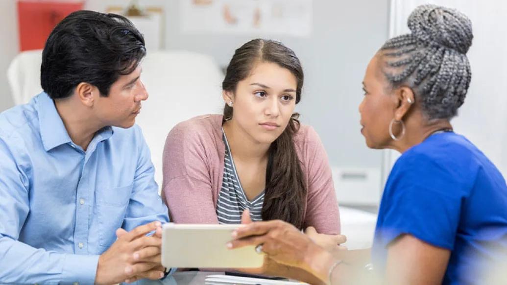 Father and daughter sitting in office talking to doctor