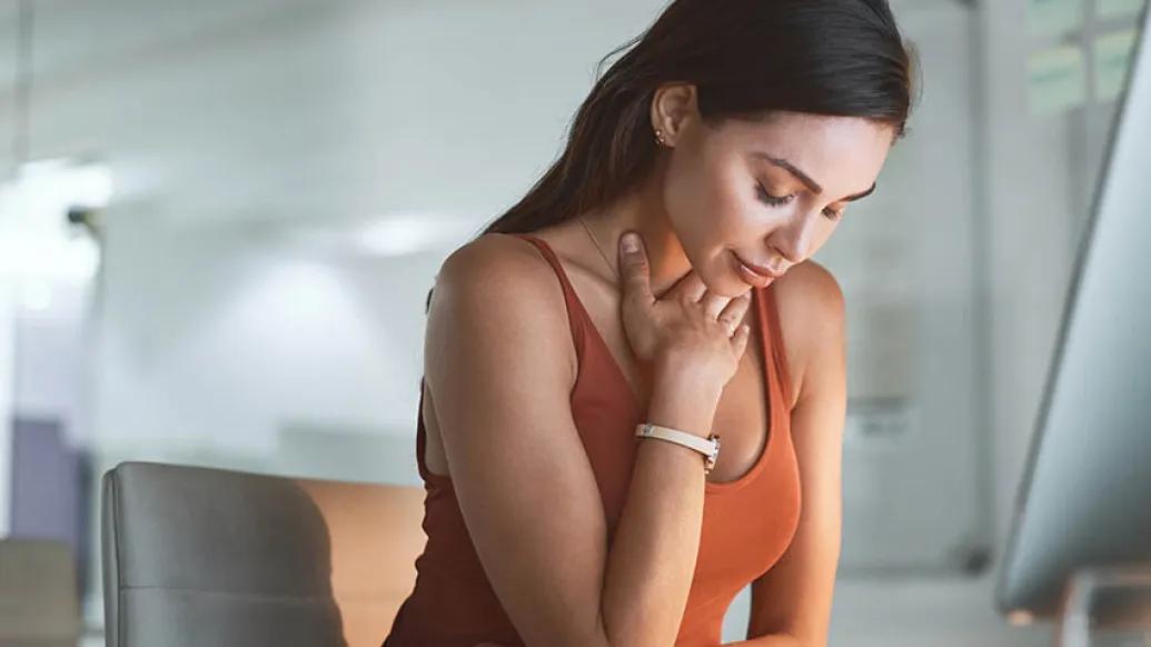 female wearing orange tank top holding her throat in discomfort and looking down