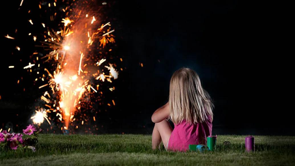 little girl sitting on grass watching fireworks