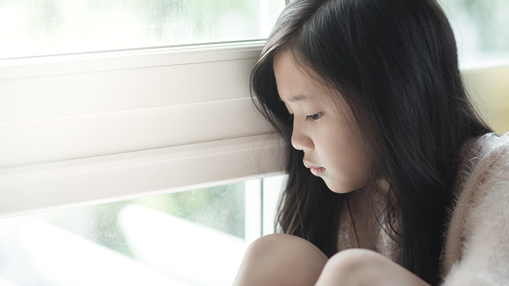 Sad young girl looking out a window