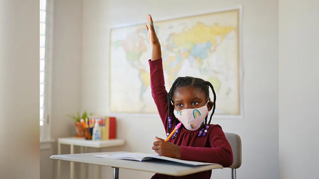 kid at school wearing mask raising hand
