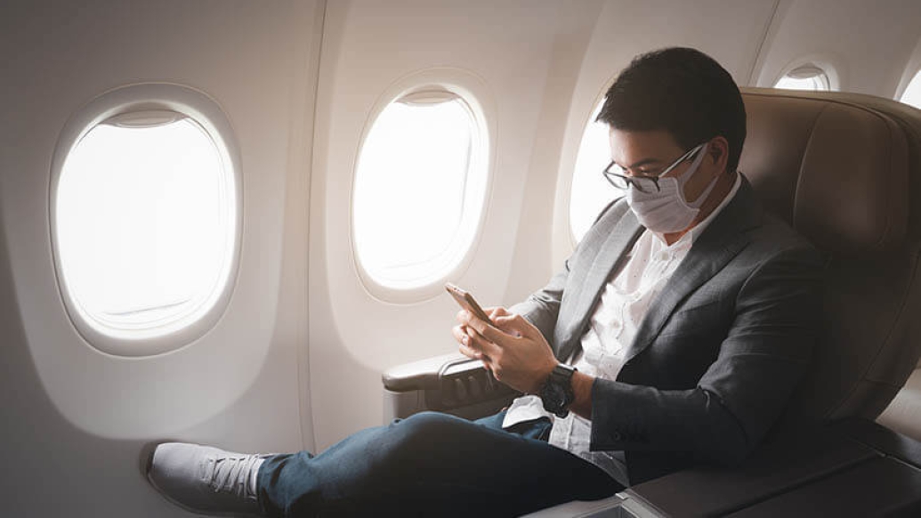 Male on airplane with mask using phone