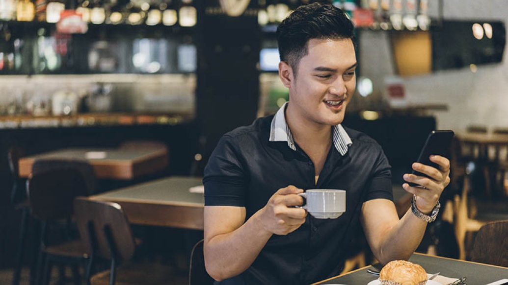 Man drinking coffee and looking at cell phone