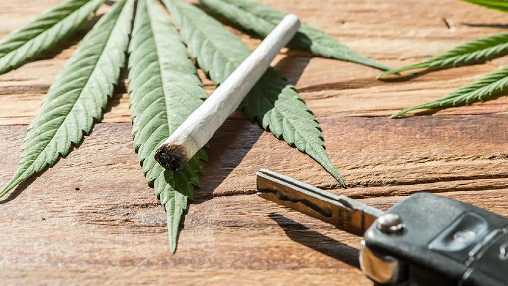 Car key and a marijuana cigarette laying on cannabis leaves