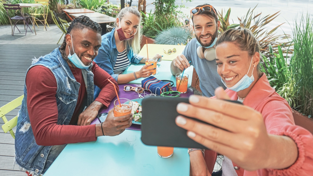 people sitting together with masks pulled down taking a selfie at a picnic table