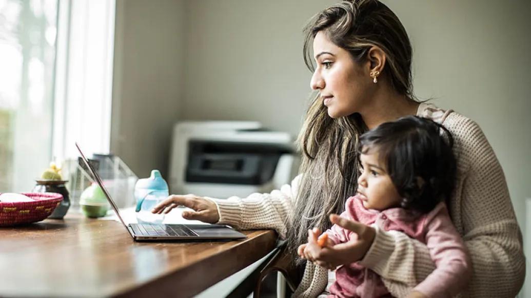 mom working on laptop with child on lap at table