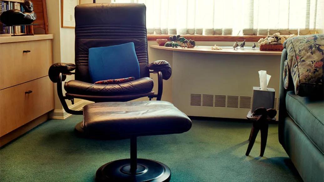 maroon office chair with blue pillow in it with foot rest and green couch next to it with green carpet on floor