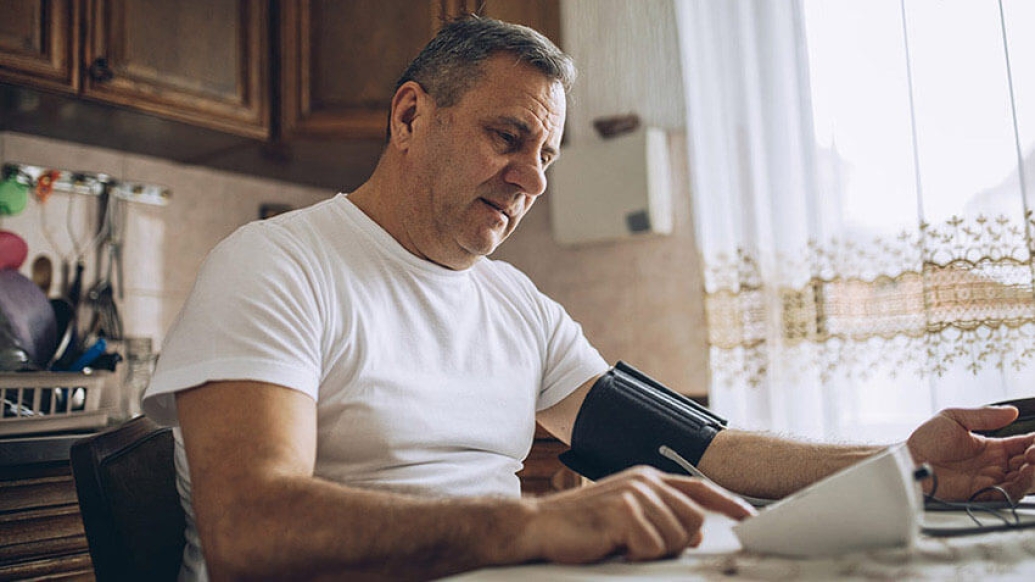Older man looking at paper in kitchen while checking blood pressure