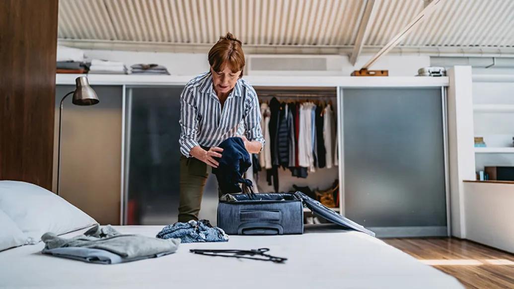 woman packing over bed in striped blue and white shirt