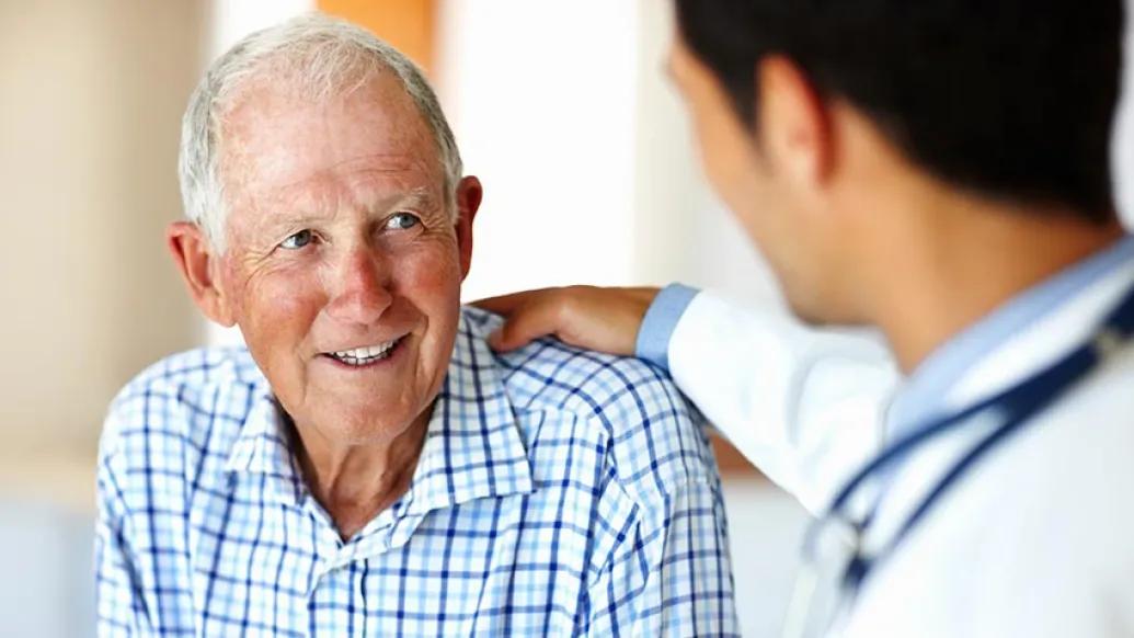 older gentleman in blue checkered shirt talking with doctor