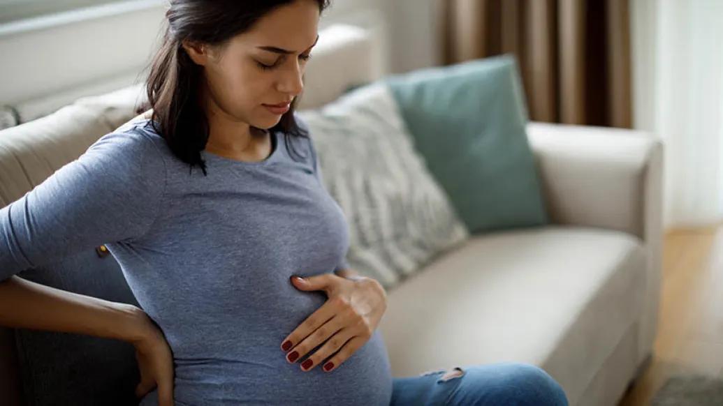 pregnant woman holding stomach on couch in pain