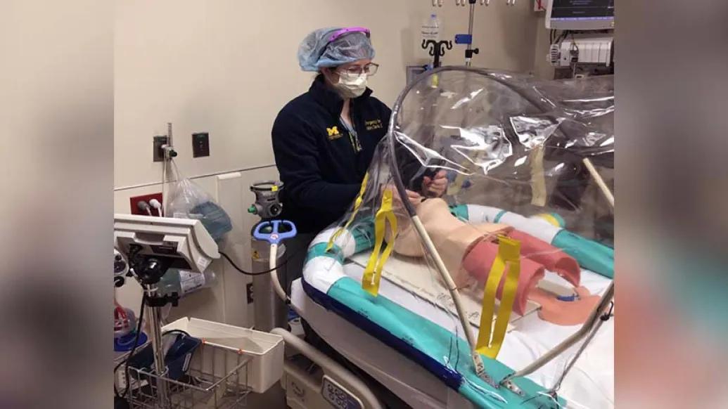 man with mask in hospital room reaching into portable negative pressure procedural tent