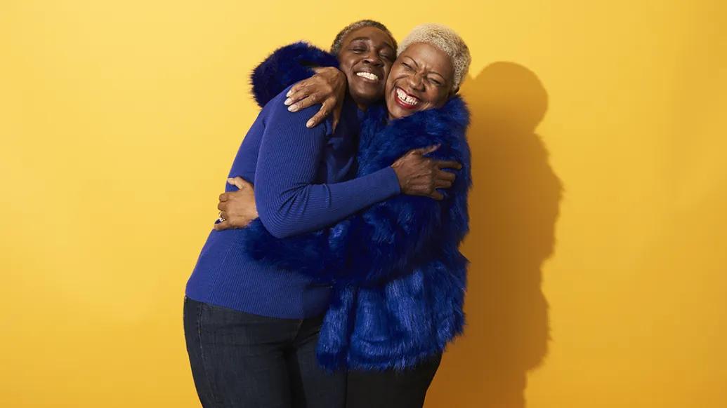 two adults hugging in yellow background wearing royal blue clothes