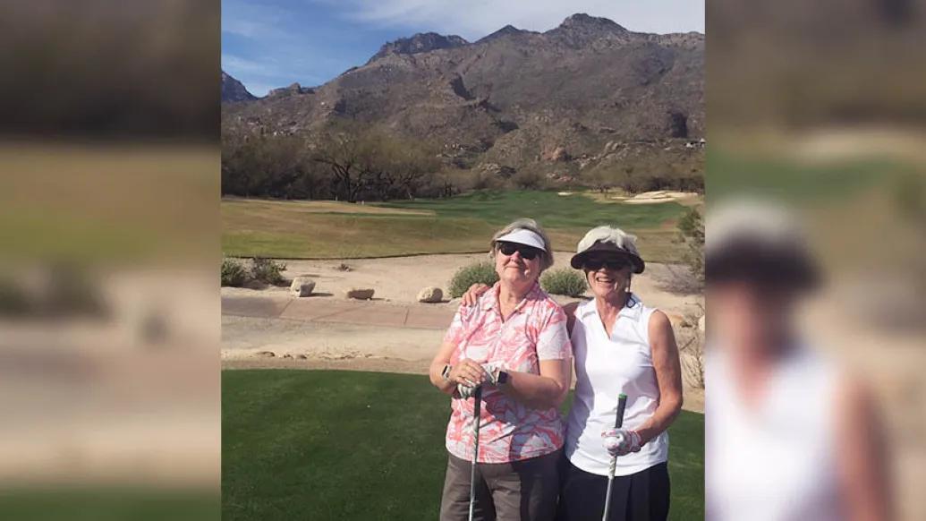 two ladies golfing in front of a mountain wearing hats